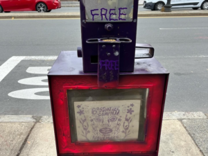 A Boston Compass newspaper box on a busy street